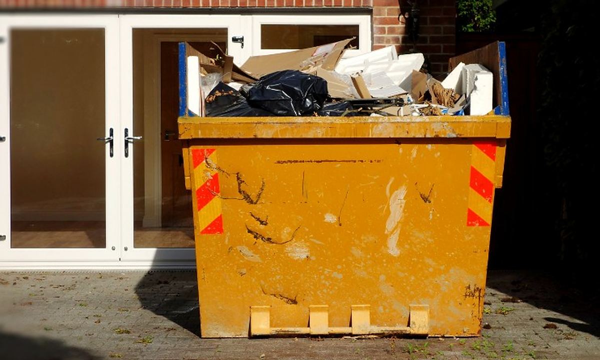 Contenedor de obra lleno de muebles y enseres frente a la puerta de una vivienda