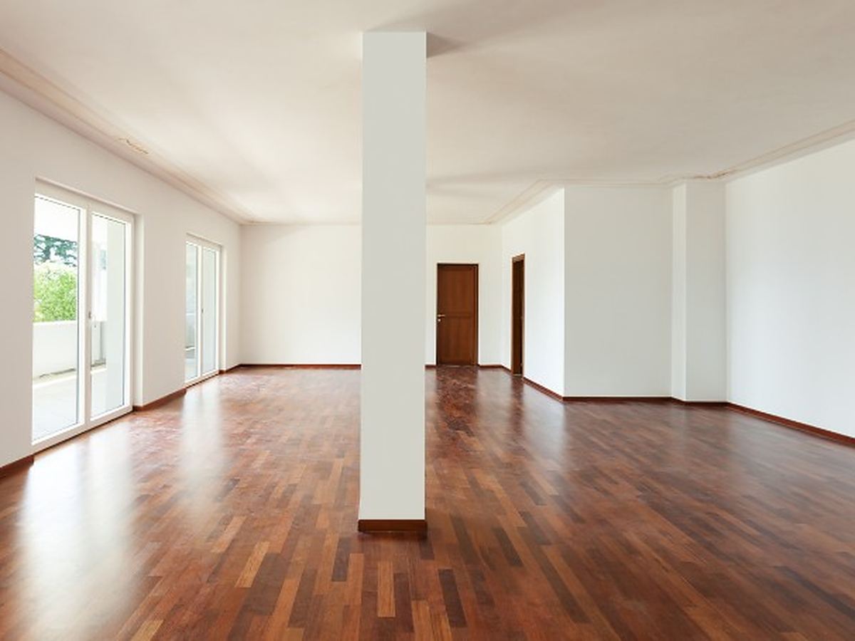 Salón amplio de un piso heredado, ya vacío, con parquet oscuro y salida a la terraza